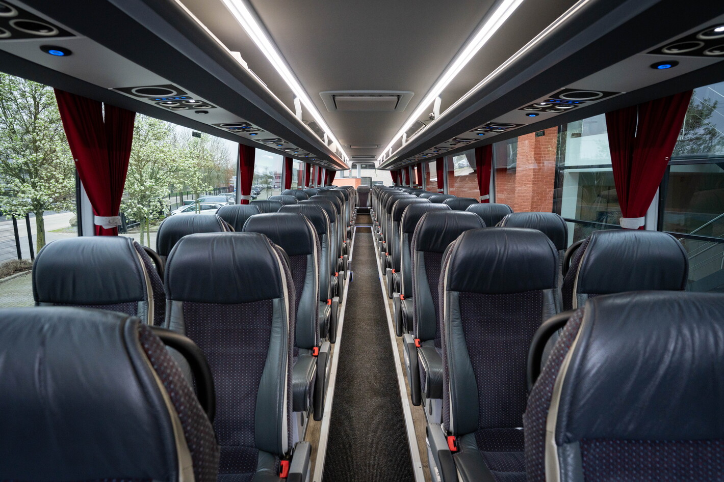 Lege touringcar met rijen grijze stoelen en verlichte plafondstrips.