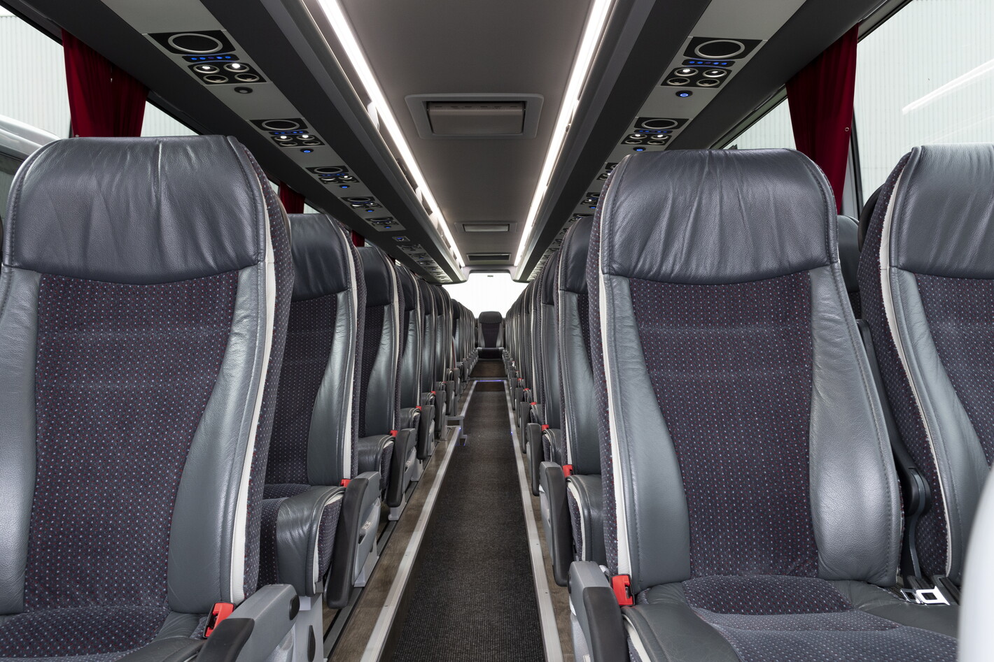 Interieur van een lege touringcar met rijen grijze stoelen en middenpad.