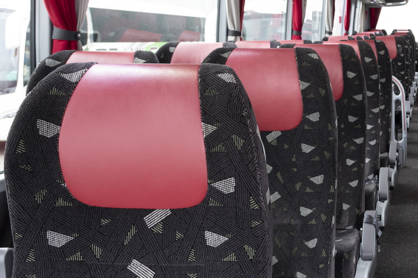 Rij busstoelen met roodzwarte bekleding, gezien van achteren.