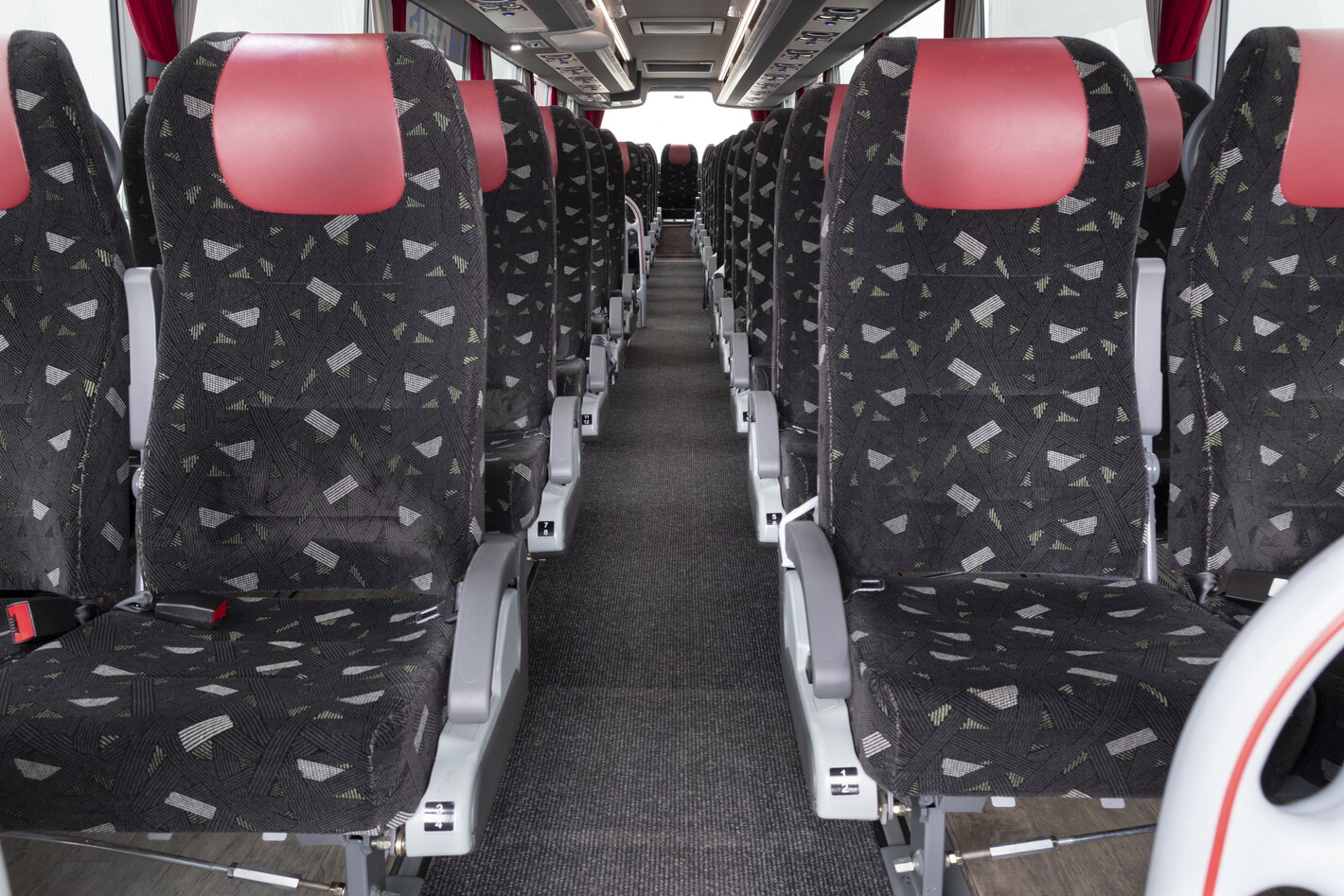 Rij lege busstoelen met roodgrijze hoofdsteunen en middenpad in perspectief