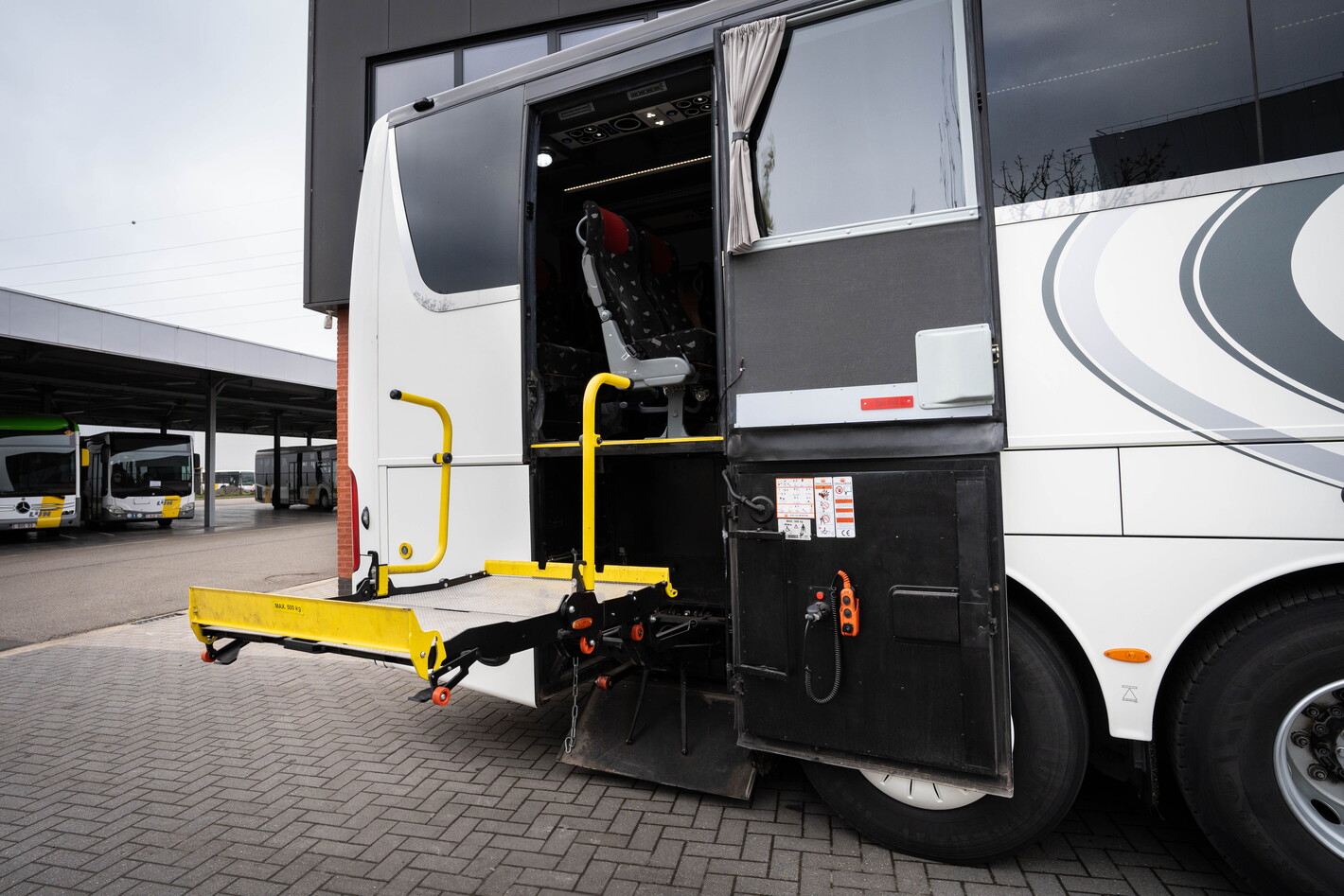 Open deur van witte touringcar met gele rolstoellift buiten op parkeerplaats