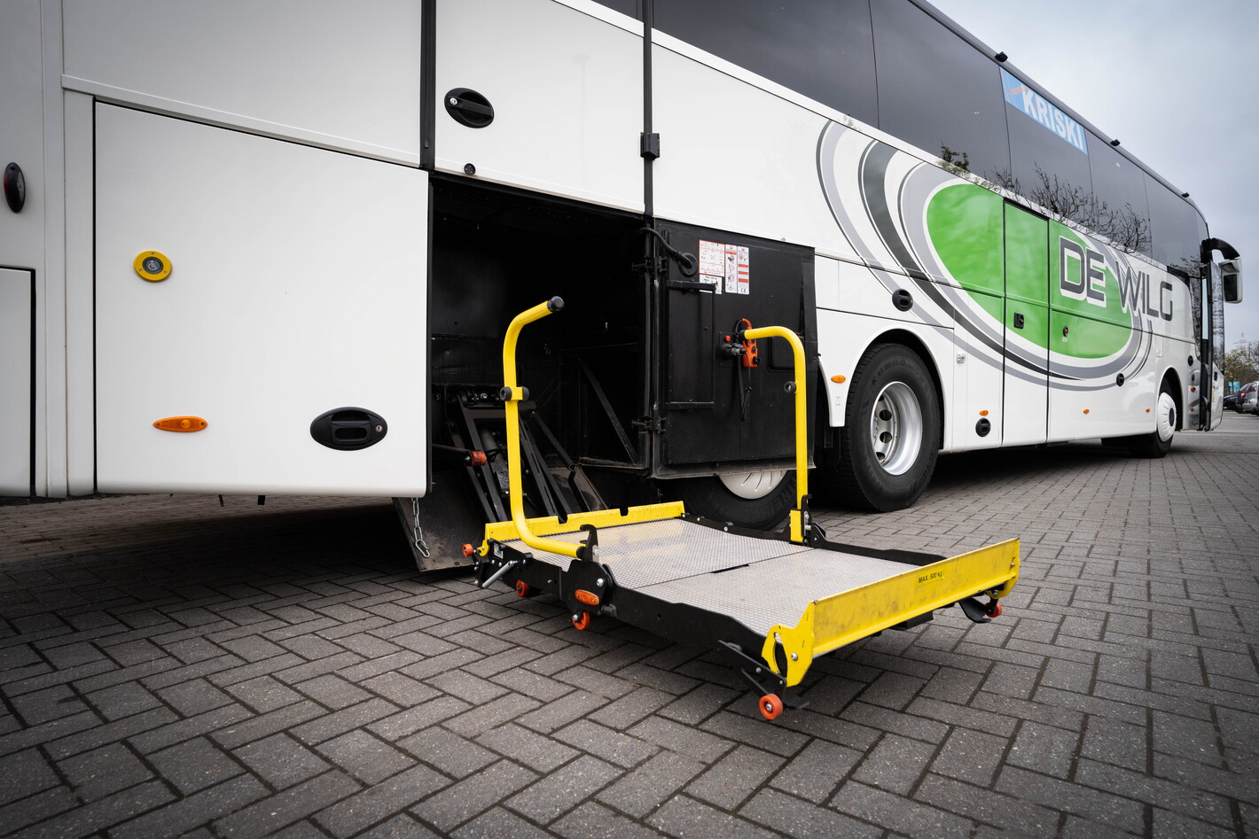 Rolstoelplatform bij instap van een witte stadsbus op klinkerstraat.