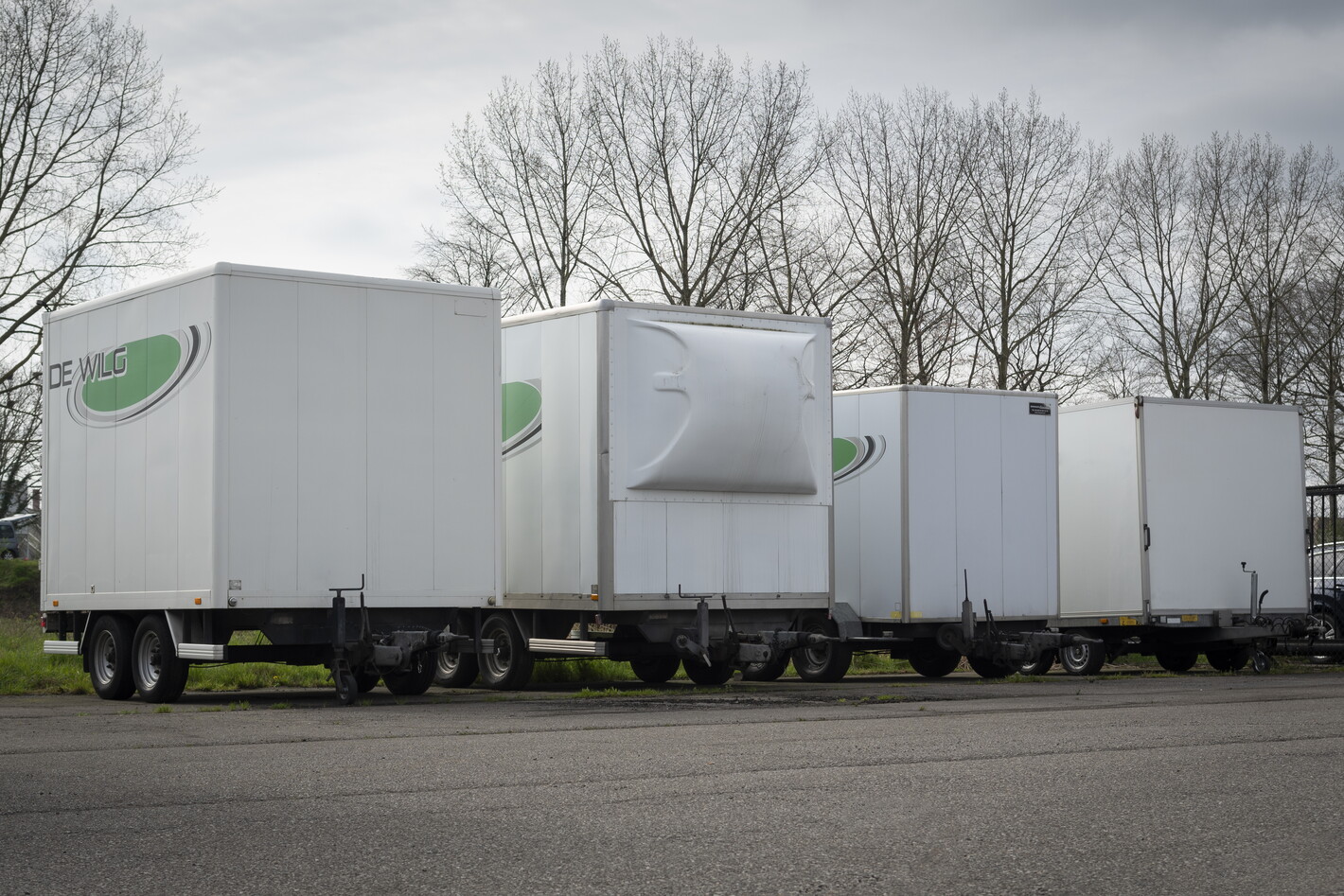 Rij witte opleggers geparkeerd op een asfaltterrein bij kale bomen