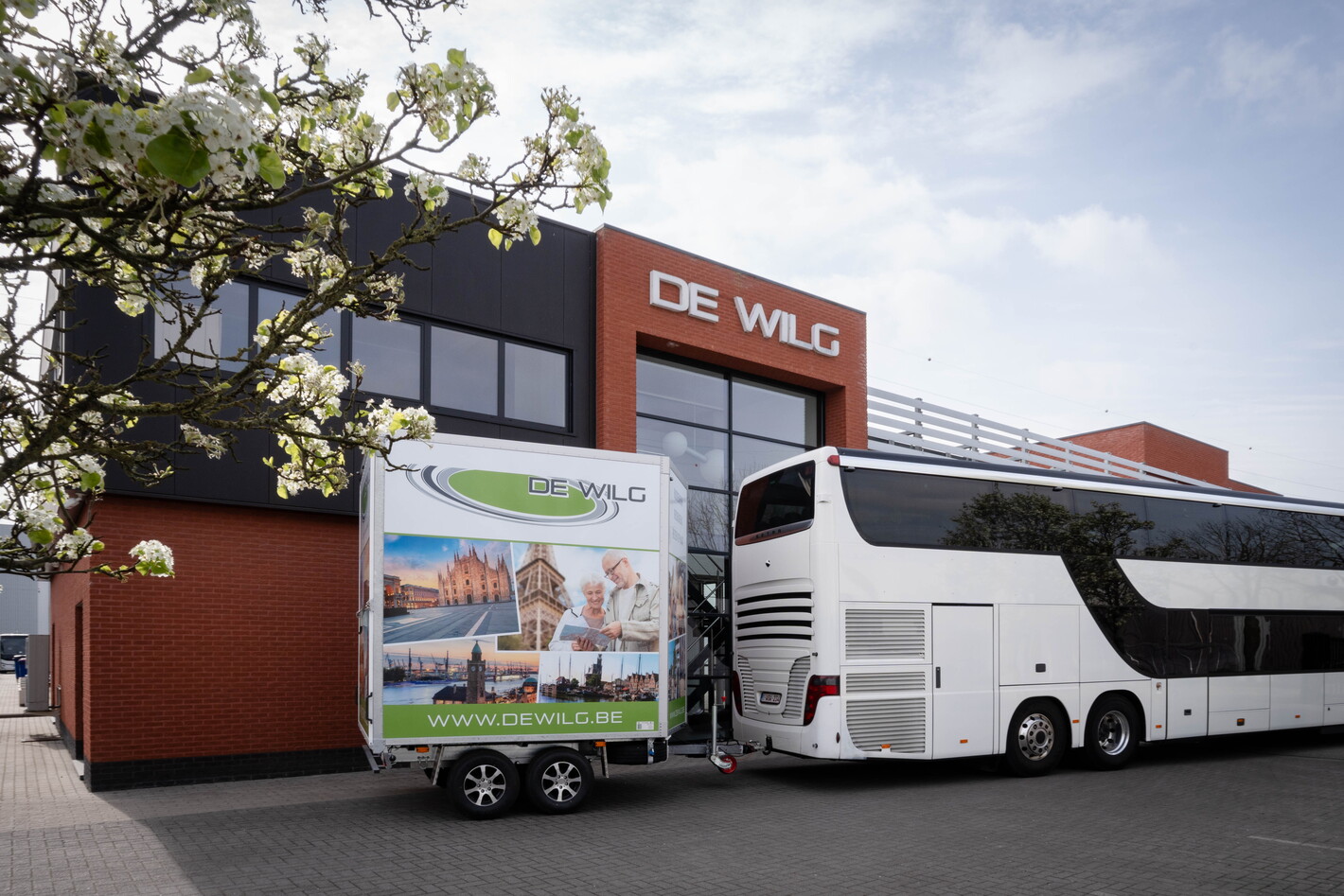 Tourbus geparkeerd naast gebouw met aanhanger met reclamebord, blauwe lucht.