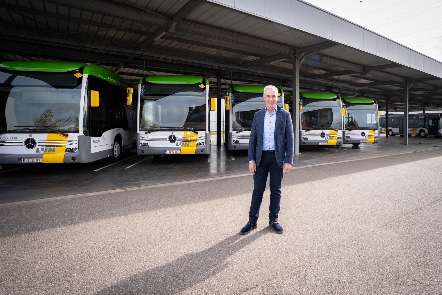 Man in pak bij busstation met geparkeerde bussen onder overkapping.