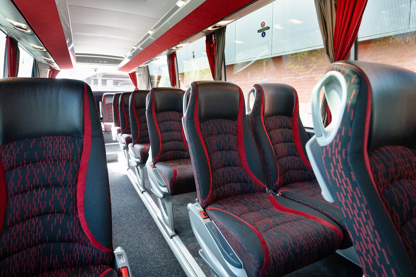 Lege bus met rijen rood-zwarte stoelen en rode gordijnen bij de ramen