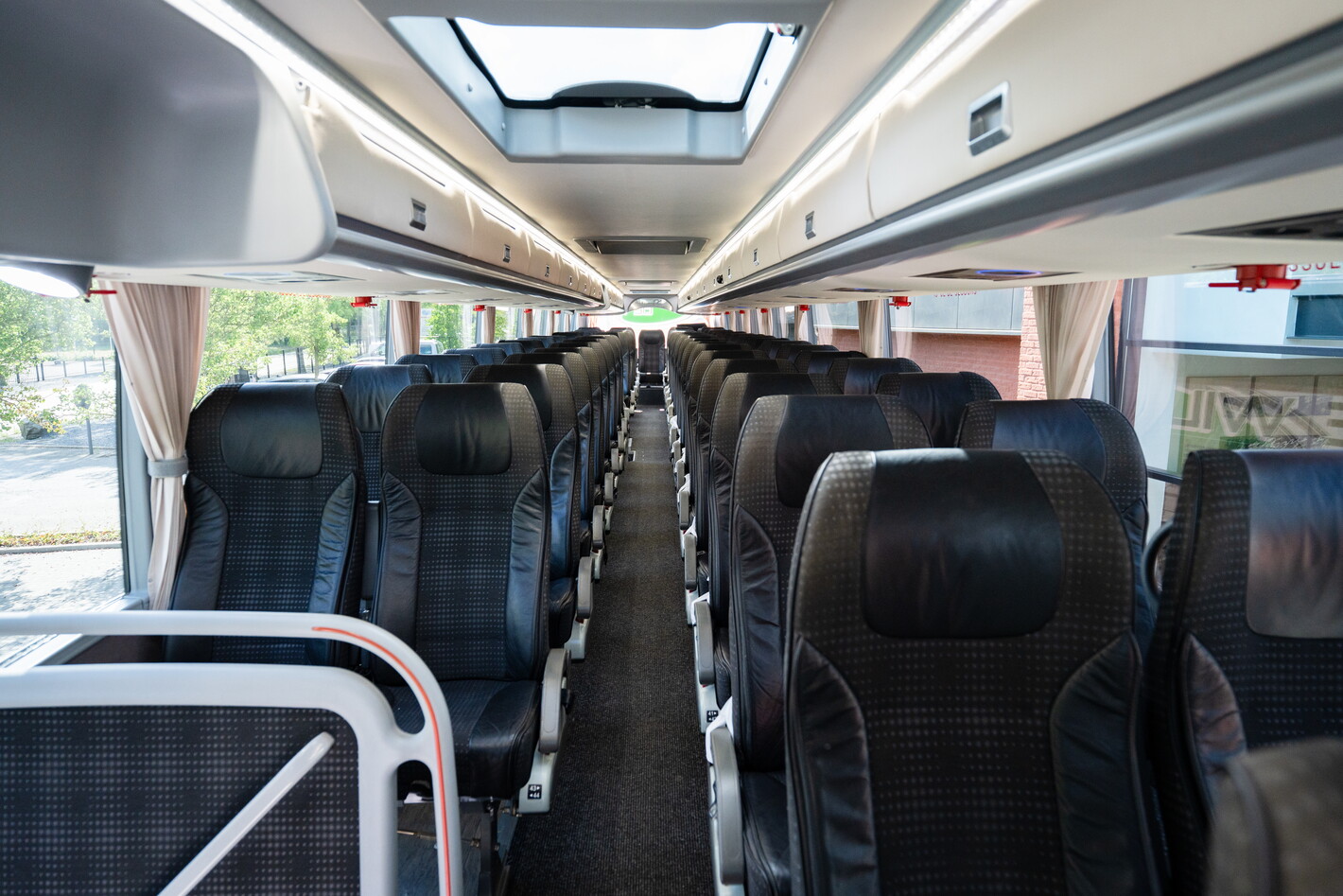 Interieur van een lege touringcar met rijen zwarte stoelen en dakraam