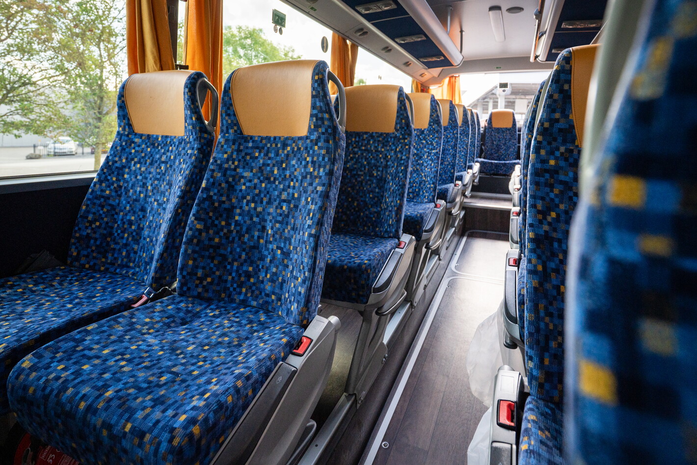 Blauwe stoelen in een bijna lege bus, met daglicht door de ramen.