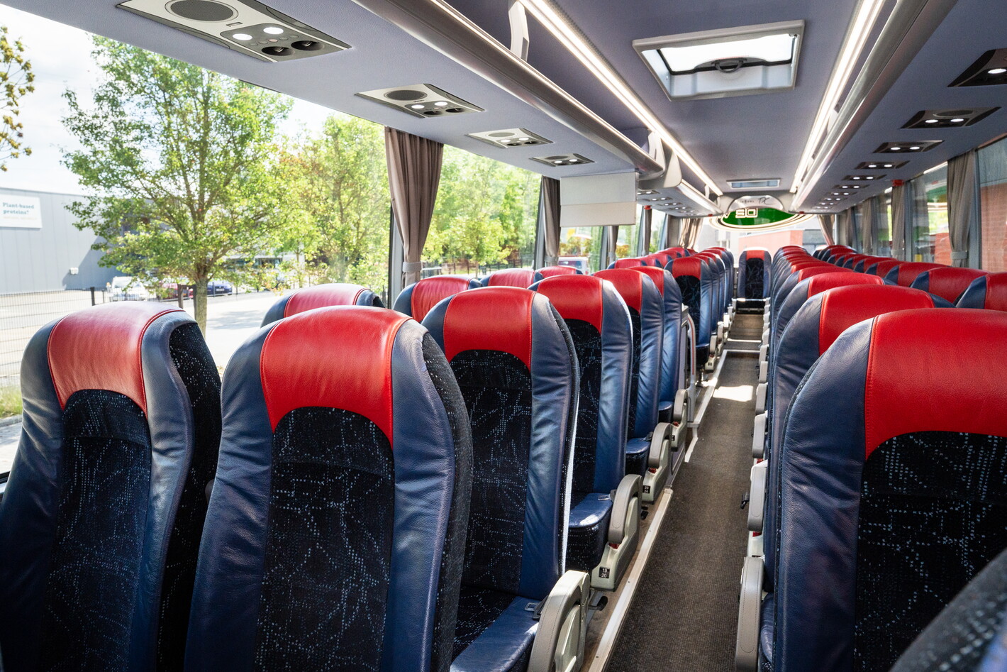 Interieur van een bus met lege blauwe stoelen en rode hoofdsteunen.