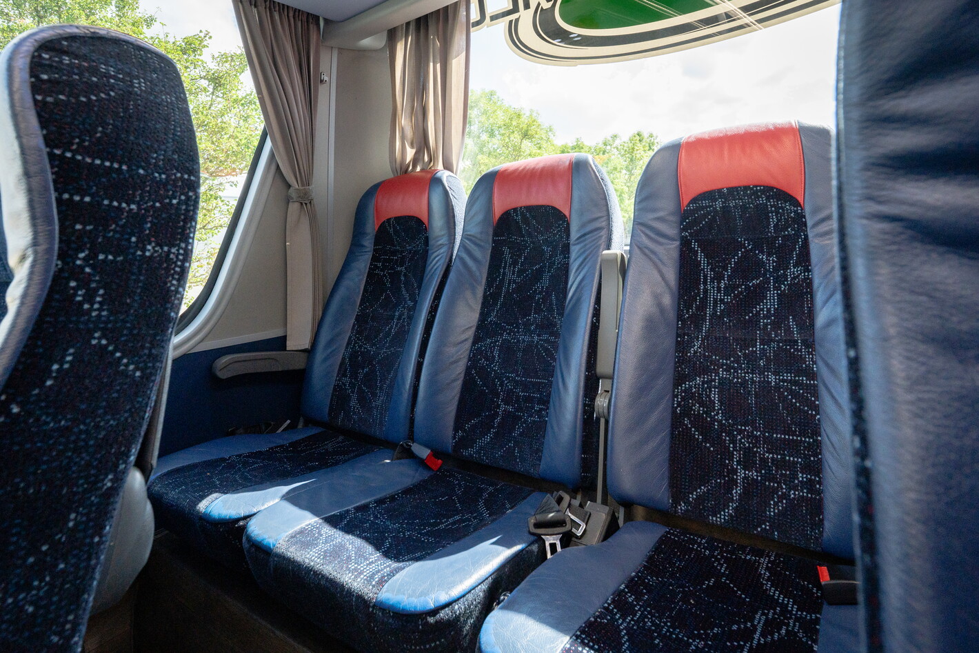 Drie blauwe busstoelen met rode randen, zonlicht door het raam