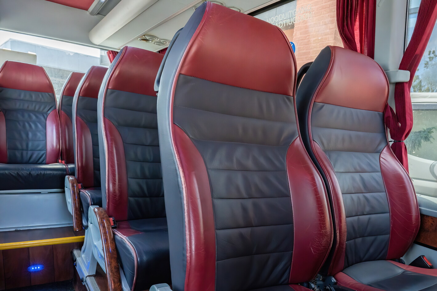 Rood-zwarte busstoelen met lederlook in het interieur, daglicht door de ramen.