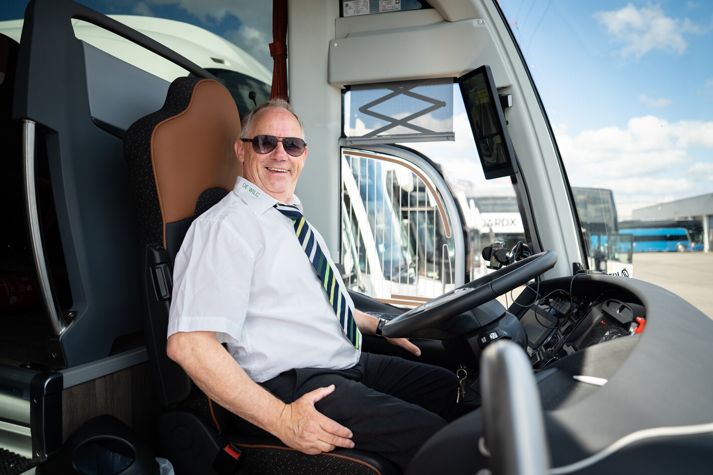 Vrachtwagenchauffeur met zonnebril zit glimlachend in de cabine bij het stuur.