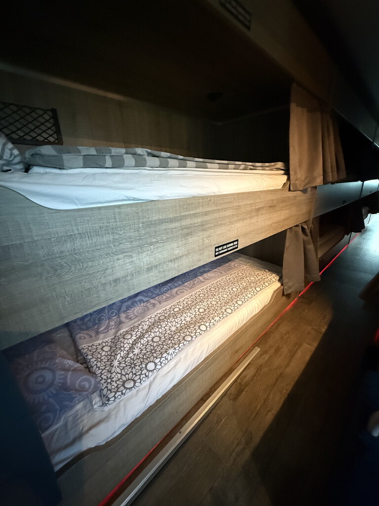 Stapels opgerolde stoffen op houten planken in een donkere opslagruimte