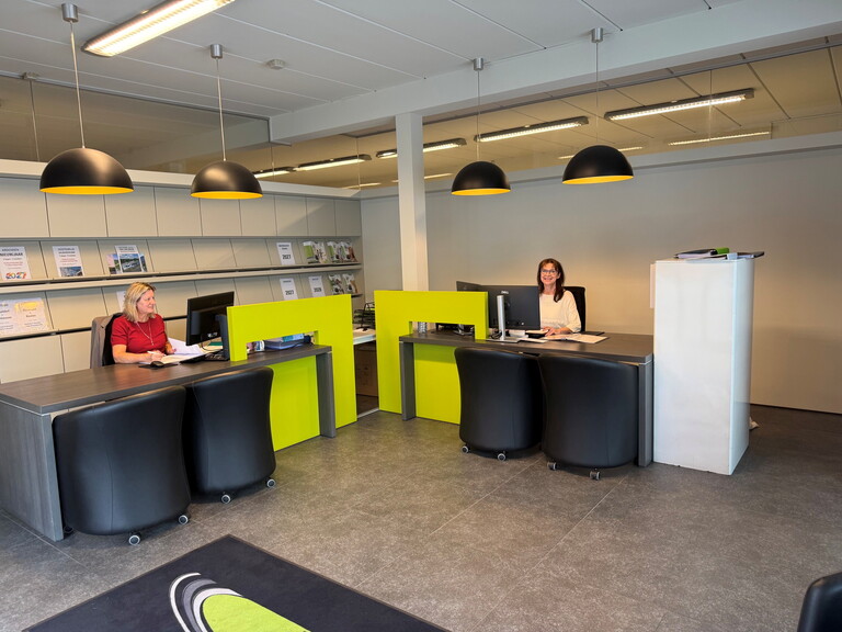 Moderne balie met twee receptionisten achter zwart‑groene toonbank in kantoorruimte